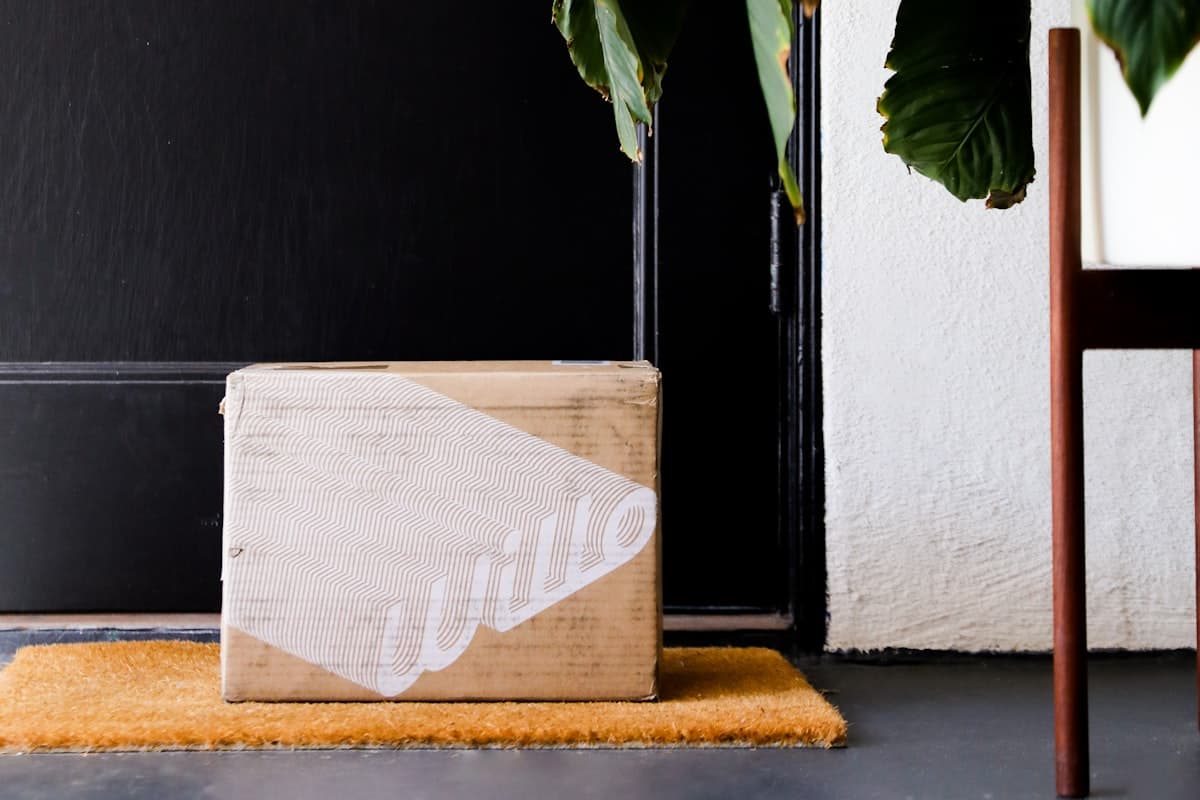 A delivery box on a doormat with a phone showing a feedback prompt